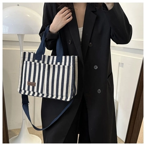 Détail du sac cabas en toile rayée avec bandoulière réglable et écusson en cuir