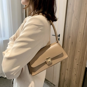 Sac baguette élégant en similicuir beige avec boucle dorée porté à l'épaule par un mannequin