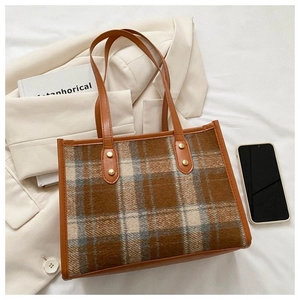 Close-up of vintage brown plaid tote bag with golden rivets and leather strap detailing