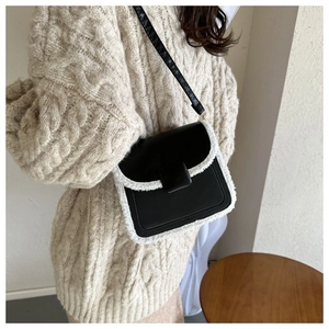 Detail of a black leather crossbody bag with white faux fur trim on a beige sweater