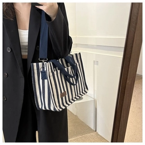 Détail du sac cabas en toile rayée bleue et blanche avec écusson logo en cuir marron