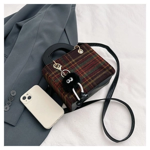 Detail of tweed plaid crossbody bag featuring decorative large-eyed fuzzy charm
