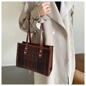Detail of plaid tote bag with brown leather handles and golden metal rivets on beige coat