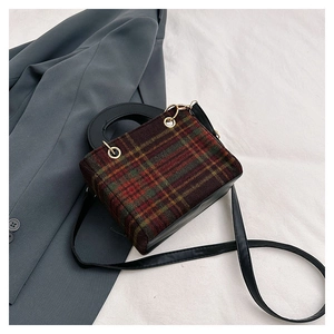 Detail of red and green plaid woolen crossbody bag with black round handle and gold hardware