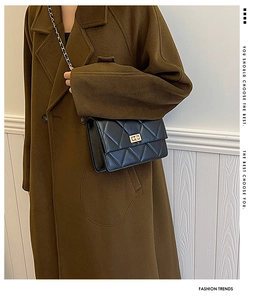 Détail d'un sac bandoulière noir matelassé avec fermoir doré sur manteau marron
