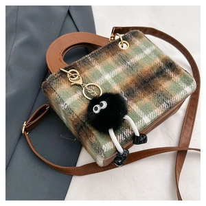 Detail of plaid wool crossbody bag with brown leather strap and fuzzy black pendant