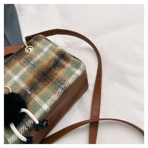 Macro detail of retro plaid wool stitching and brown leather texture on a crossbody bag