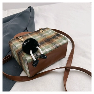 Detail of plaid wool crossbody bag with a cute plush charm on a cream fabric base