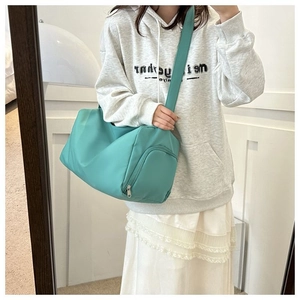 Sac bandoulière cylindrique en nylon bleu sarcelle montré dans un miroir avec modèle
