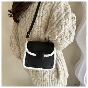 Detail of black crossbody bag featuring contrast faux shearling trim and metal clasp buckle