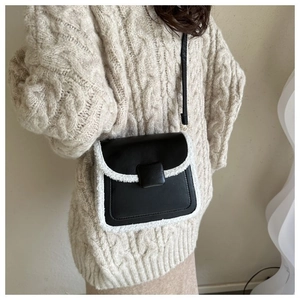 Detail of black crossbody bag with white shearling trim on a beige knit sweater
