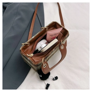 Plaid woolen tote bag with leather handles and black plush ball charm on white background