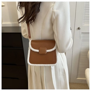 Close-up of brown faux leather crossbody bag with white shearling trim and buckle