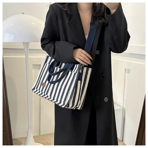 Détail du sac fourre-tout en toile rayé bleu et blanc avec logo en cuir et bandoulière amovible