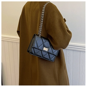 Détail d'un sac matelassé noir avec fermoir doré porté sur un manteau en laine