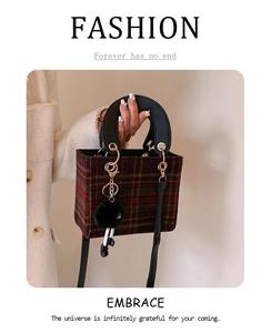 Detail of red plaid wool handbag featuring black round handles and a cute doll charm