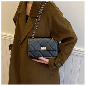 Détail du sac bandoulière matelassé noir avec fermoir doré sur manteau marron