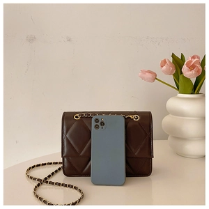 Gros plan d'un sac à bandoulière en cuir marron avec chaîne à côté d'un téléphone mobile