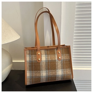 Detail view of plaid tote bag featuring woolen fabric and brown leather straps