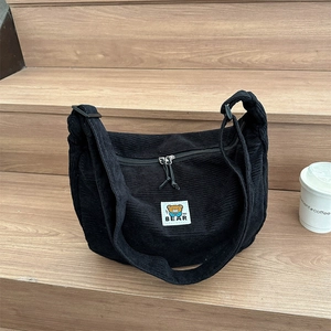 Black corduroy crossbody bag with cartoon bear patch and zipper closure on wooden steps
