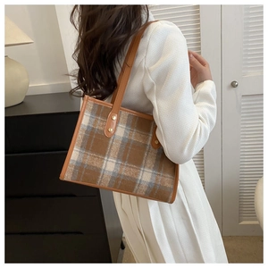 Detail of plaid tweed tote bag with brown leather straps and gold rivets on a model