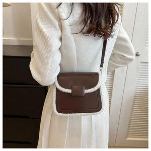 Detail van bruine crossbodytas met witte pluchen bies op een witte blazer achtergrond