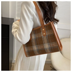 Detail of checkered tote bag featuring brown leather trim and golden rivet accents