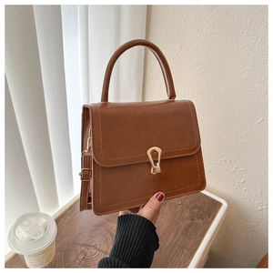 Detail of a brown leather crossbody bag featuring a unique gold teardrop metal buckle