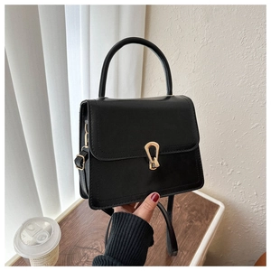 Detail of black leather crossbody bag featuring a distinctive golden horseshoe buckle clasp