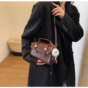 Detail of vintage brown patent leather handbag with gold buckle and white plush charm