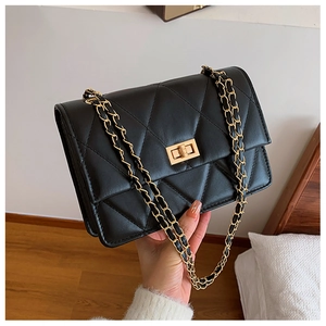 Détail d'un sac matelassé noir avec fermoir doré tournant et bandoulière chaîne
