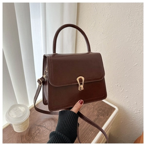 Detail of a brown leather crossbody bag featuring a gold horseshoe metal clasp and handle