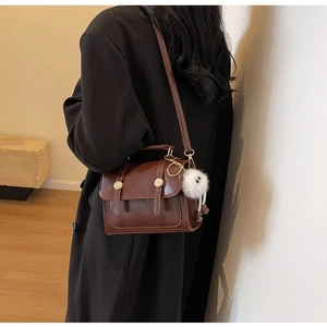 Detail view of a vintage brown leather crossbody bag with a white fuzzy monster charm