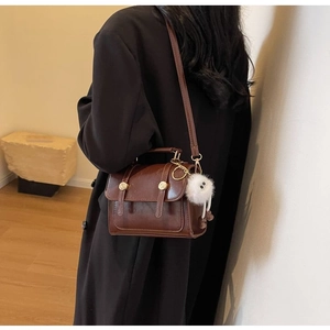 Detail of vintage brown crossbody bag with metal rivets and fluffy plush pendant charm
