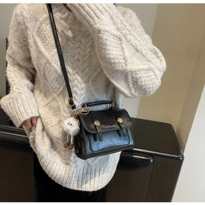 Close-up of black vintage leather mini crossbody bag with a cute white plush doll charm