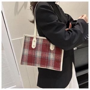 Detail of red plaid tweed tote bag with leather trim and gold rivets on a black blazer