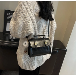Close-up of retro black faux leather bag with glossy texture and white plush charm detail