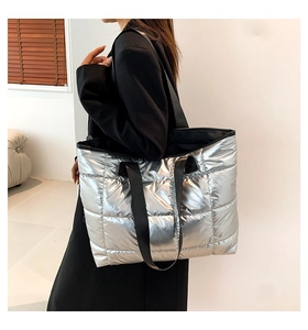 Bolso tote acolchado plateado con asas negras llevado por una modelo con traje de oficina