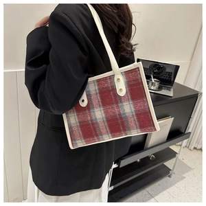 Detailed close-up of a red and white plaid wool tote bag with cream leather trim and gold studs