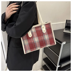 Detail of red and grey plaid tote bag featuring cream leather trim and gold rivet accents