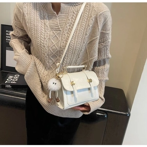 Detail of cream mini crossbody bag with gold buckle and cute white plush doll keychain