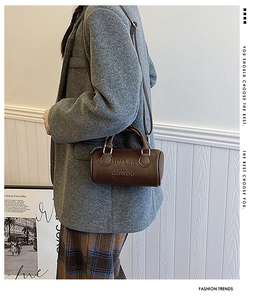Detail of coffee brown embossed leather barrel bag worn with a wool coat and checkered pants