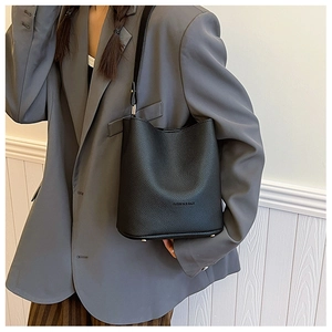 Detail of black pebbled leather bucket bag with gold studs and embossed fashion text
