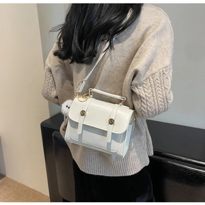 White structured square crossbody bag with top handle and fluffy pompom detail shown on model