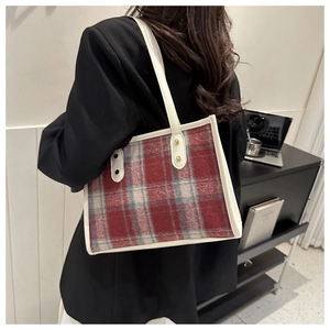 Detail of red plaid tote bag with cream leather straps on a model wearing black blazer
