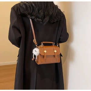 Detail of vintage brown leather crossbody bag with top handle and plush monster charm