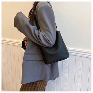 Detail of black pebbled leather bucket bag shown from side on model in office setting