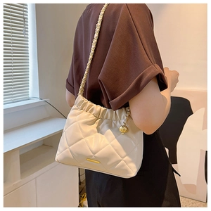 Close-up of quilted cream bucket bag with gold chain strap and metal ball pendant detail