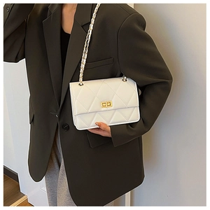 Sac bandoulière matelassé blanc avec chaîne dorée porté sur une veste de blazer verte