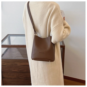 Brown pebbled leather bucket bag with adjustable strap shown on model shoulder